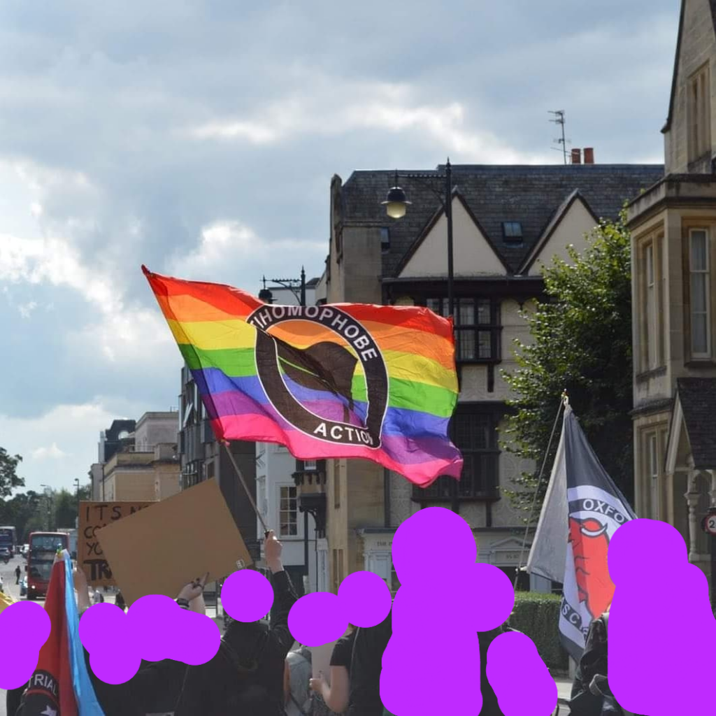 A rainbow anti homophobe action flag being flown above a group of protesters marching down a street