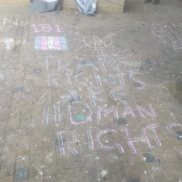 Coloured chalk writing on the ground including the numbers 181, the trans anarchy symbol and the slogan "trans rights are human rights"