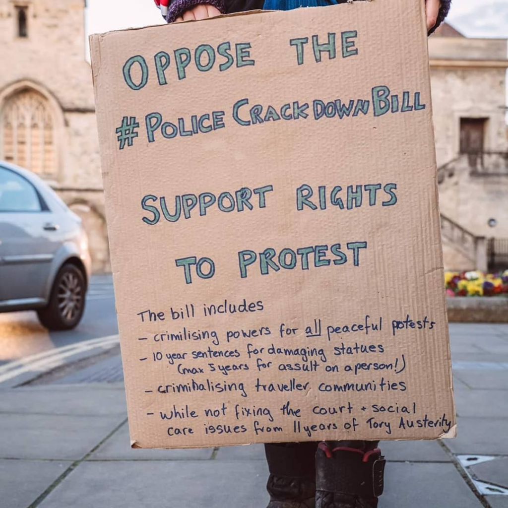 Cardboard handwritten sign in blue writing that says " Oppose the #Police Crackdown Bill, support the rights to protest, This bill includes, criminalising powers for all peaceful protests, 10 year sentences for damaging statues (max 5 years for assault on a person!), while not fixing the court and social care issues from 11 years of Tory austerity