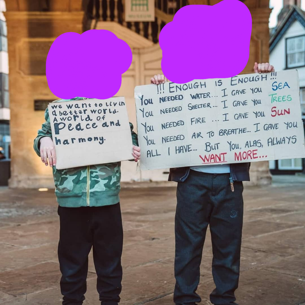 2 people holding carboard signs. The first sign says "we want to live in a better world. A world of peace and harmony." and the second sign says "Enough is Enough!!! You needed water I gave you Sea, You needed shelter I gave you trees, You needed fire I gave you sun, You needed air to breathe I gave you all I have But you always want more...
