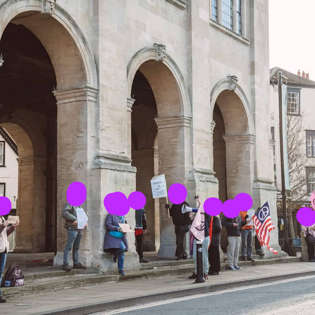 Group of people standing in front of stone arches holding protest signs and flags