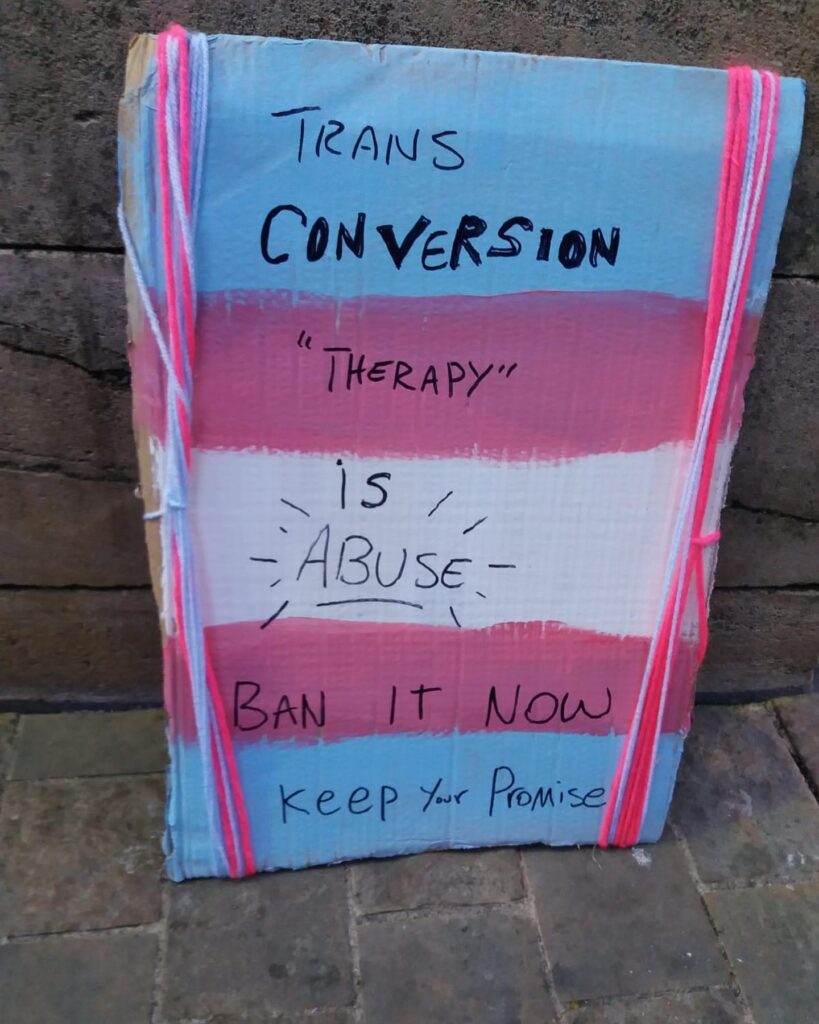 Sign with "Trans conversion "therapy" is abuse Ban it Now keep your promise" written on it