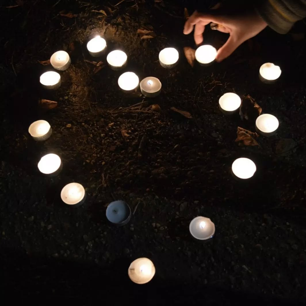 A hand placing a tealight on the ground, where more tealights are in the shape of a heart.