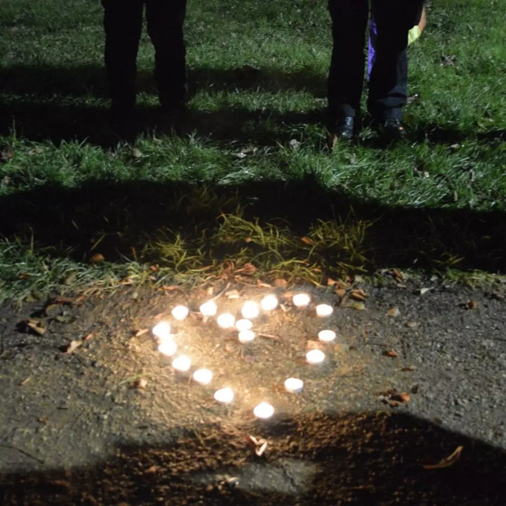 Tealights arranged on the ground in the shape of a heart and people standing around it