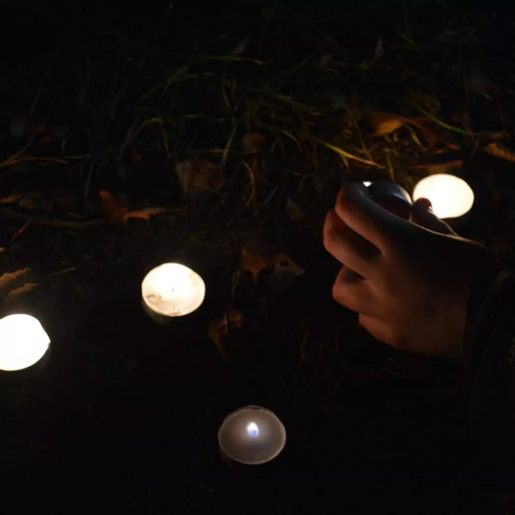 A hand lighting a tealight from another that is lying on the ground.