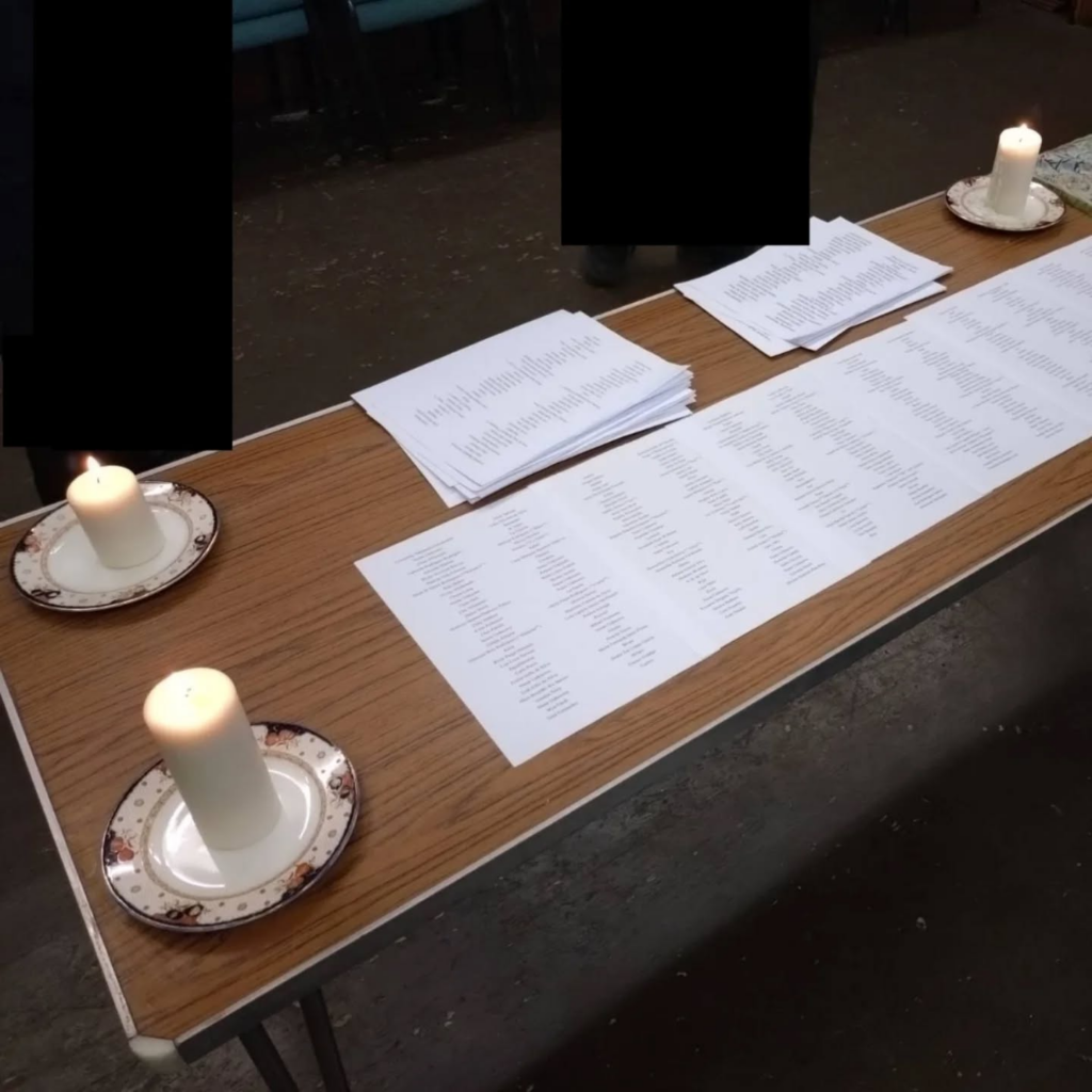 A table with four candles on it as well as printed lists of the names of those who died this year.