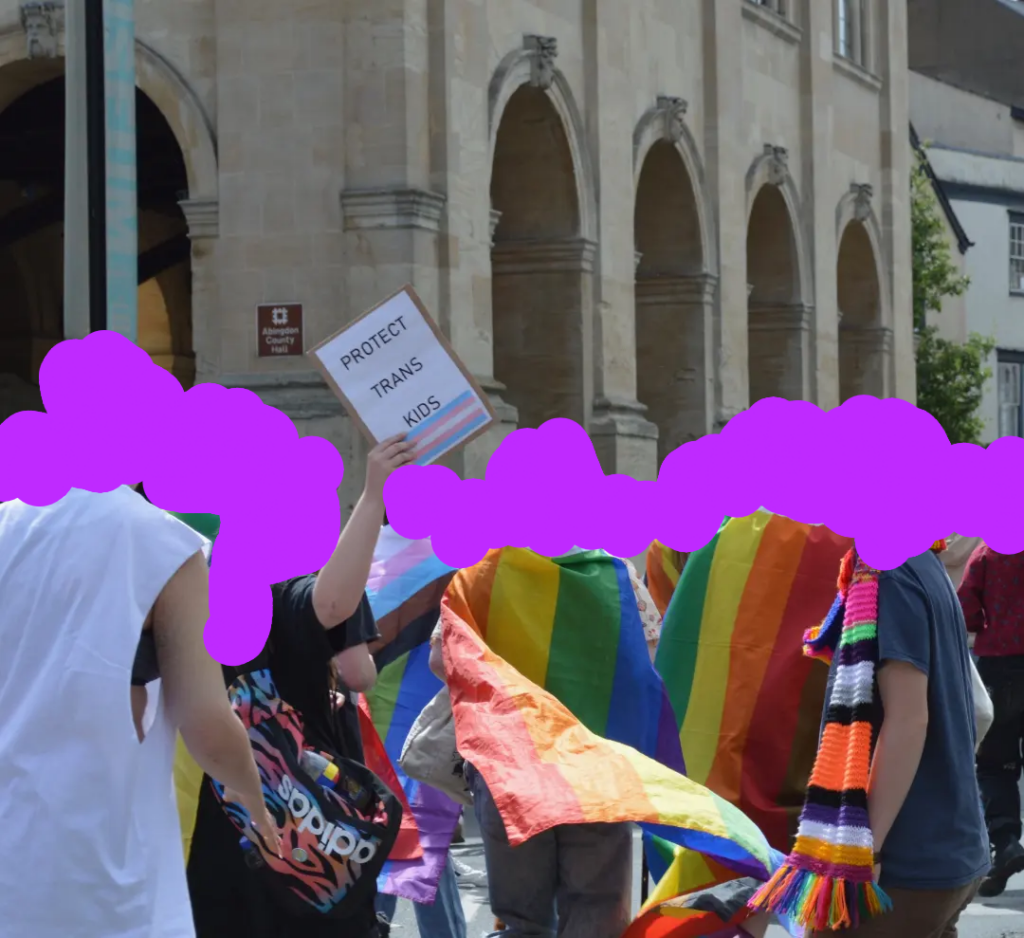 Group of people marching in the street with rainbow flags and a sign that says "protect trans kids"