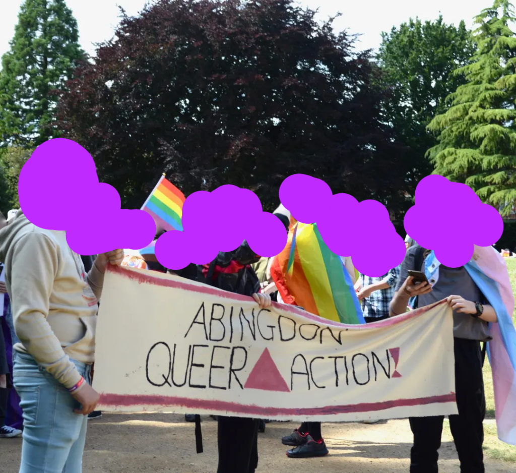Group of people holding a pink and black abingdon queer action banner and rainbow flags