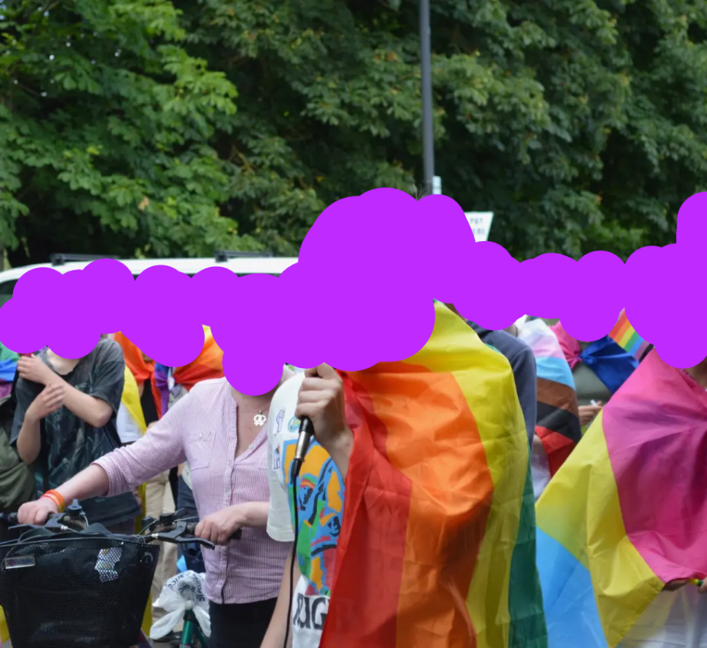 A group of people in a pride parade with queer flags including one with a microphone